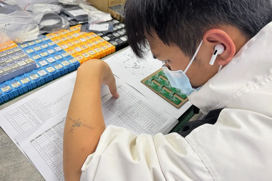 An engineer reviewing a bill of materials against a populated PCB panel
